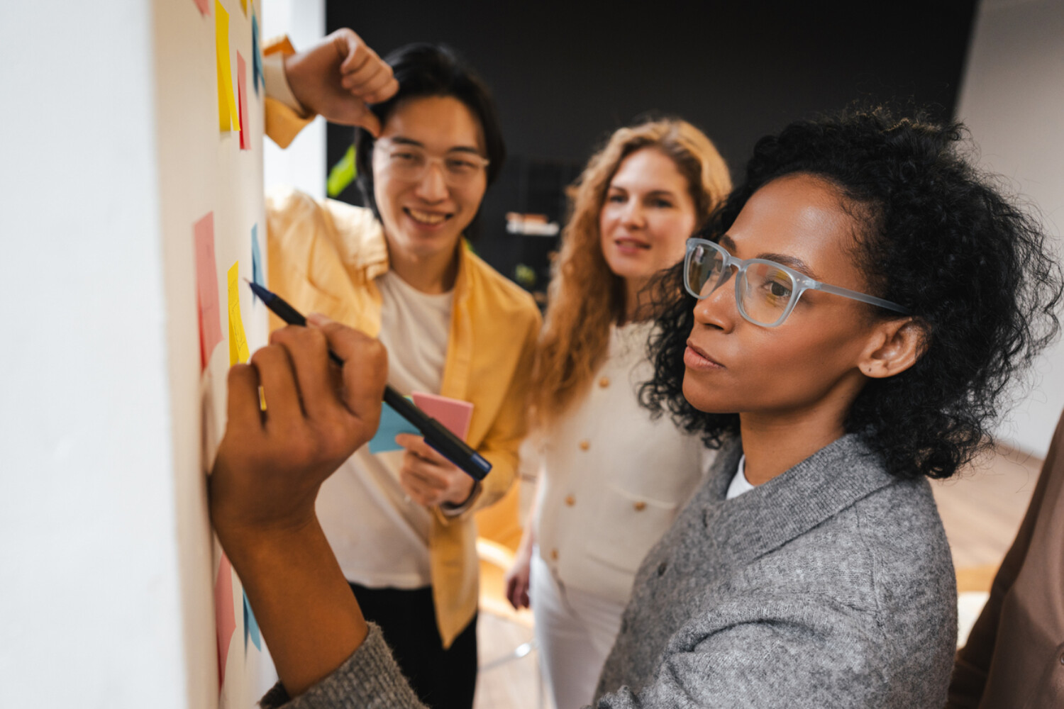 Diverse group of smiling multinational business team collaborating, brainstorming session, taking notes on sticky notes. Teamwork concept