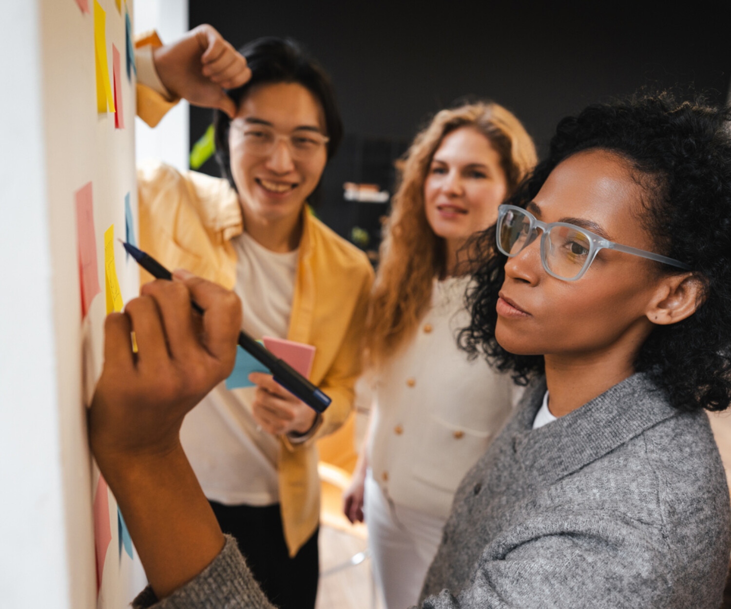 Diverse group of smiling multinational business team collaborating, brainstorming session, taking notes on sticky notes. Teamwork concept